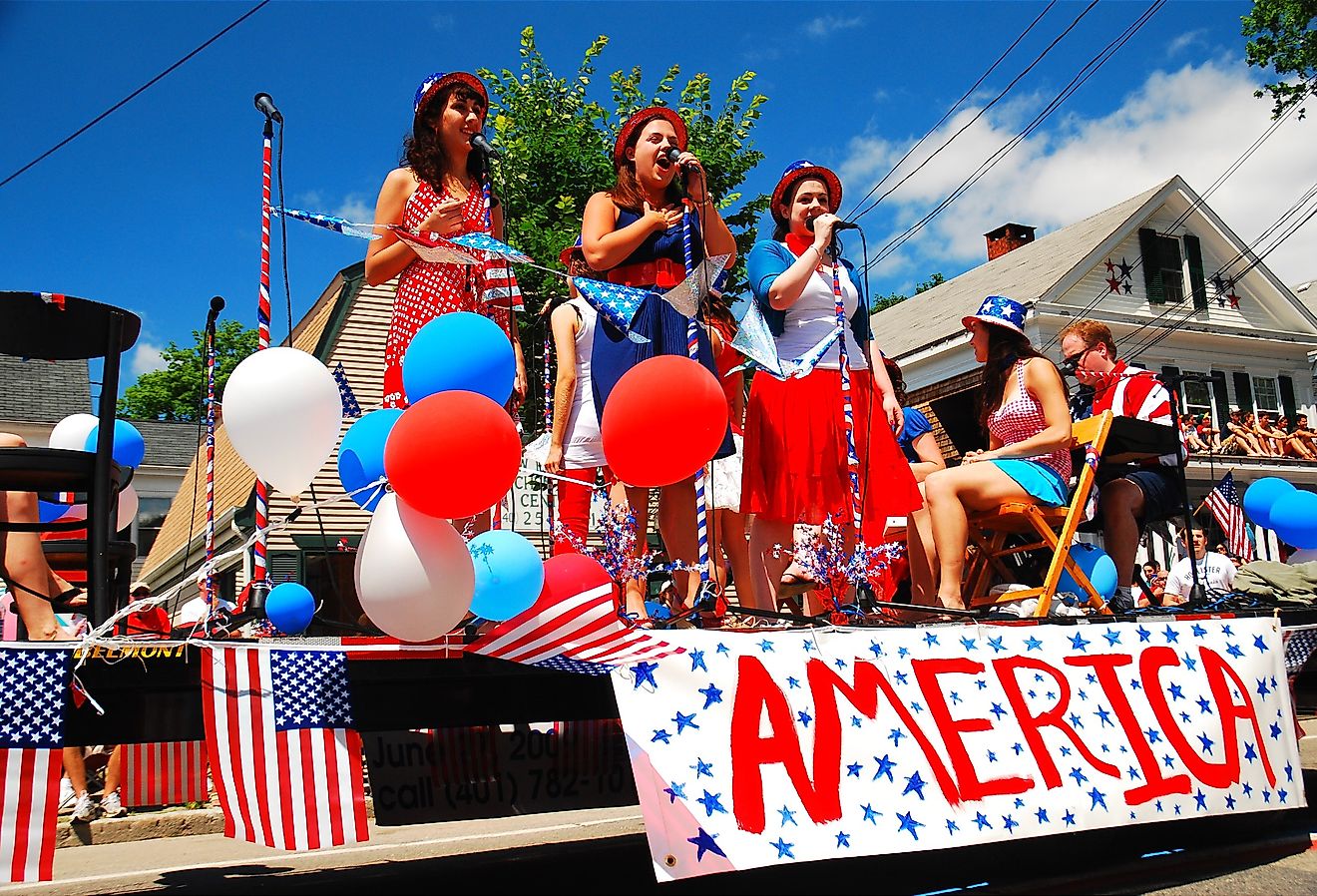 Three teenage girls sing patriotic tunes while traveling on a float during a Fourth of July parade in Bristol, Rhode Island. Image credit James Kirkikis via Shutterstock